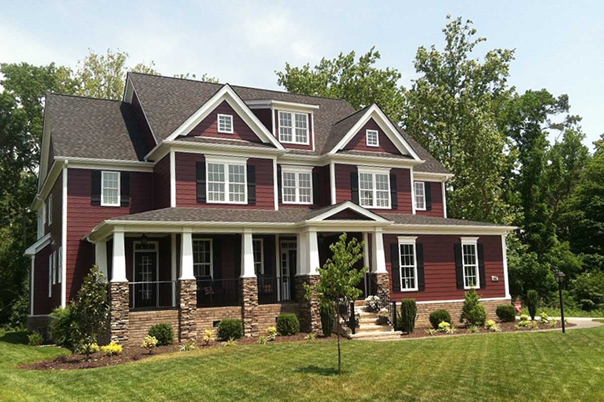 House plan exterior: Two-story home with wraparound porch, stone accents, dormers, and multiple gables.