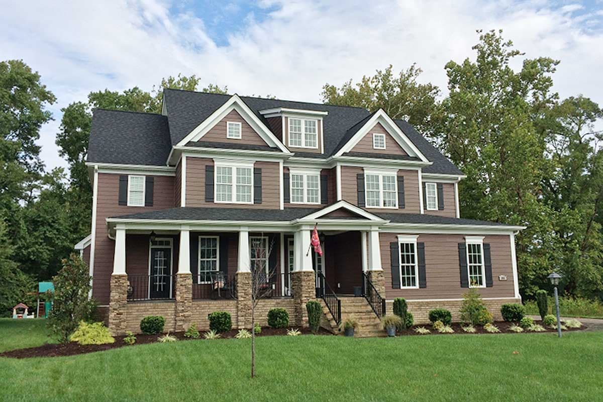 House plan exterior. Two-story home with a front porch, gables, and multiple dormers. Features dark roof and stone and siding facade.