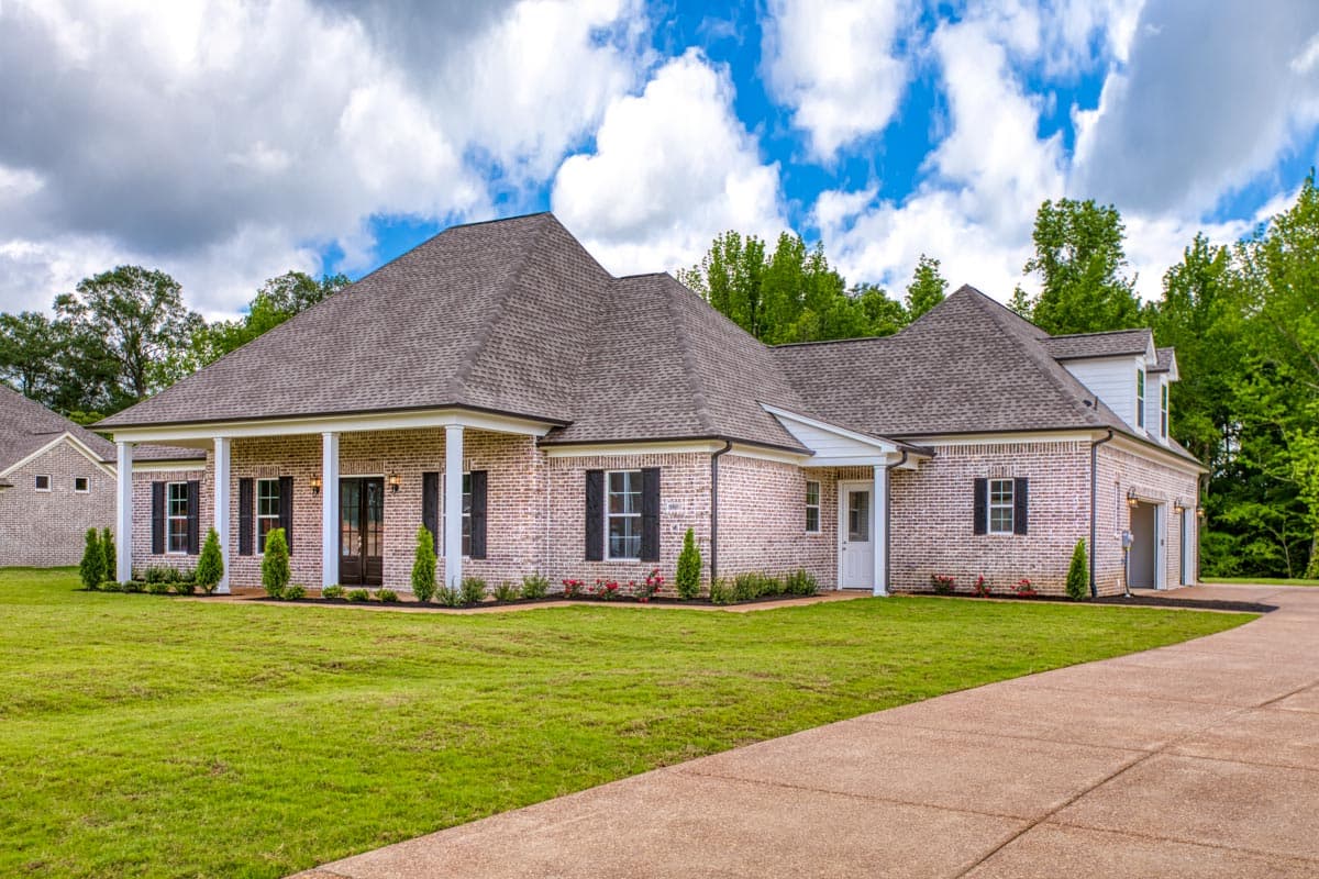 House plan exterior: One-story brick home with a covered front porch, gabled dormers, and a side-entry three-car garage.