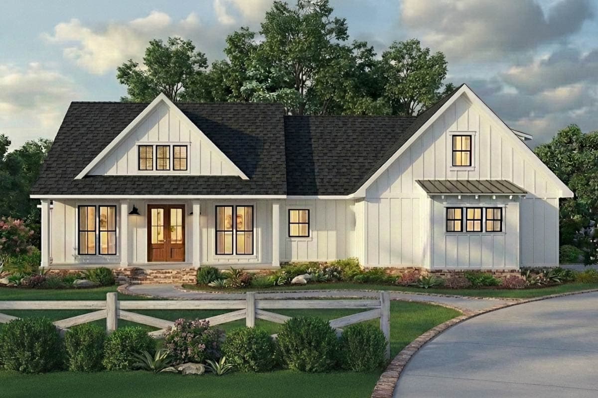 A white farmhouse with a black roof, front porch, and wooden fence. The house is surrounded by lush green landscaping and a curved driveway.