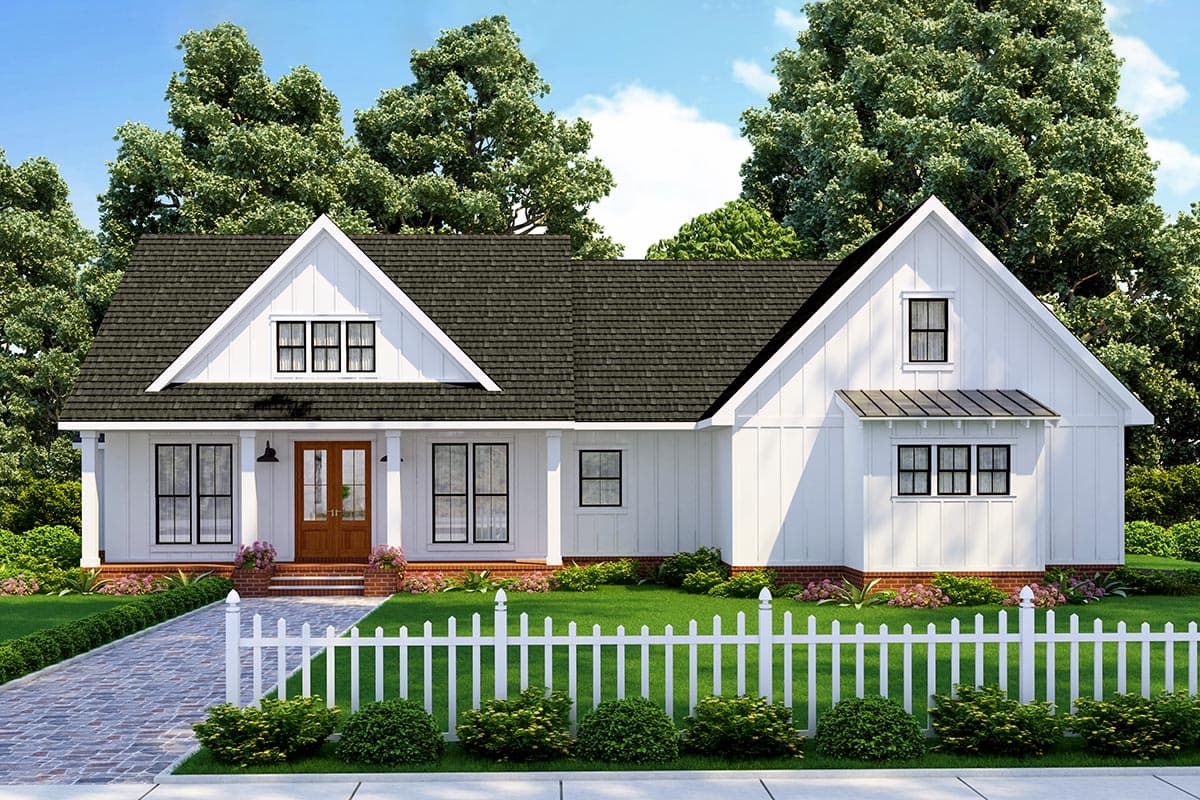 A white farmhouse with black framed windows, a dark shingled roof, and a white picket fence in front. Lush green trees and bushes surround the house.