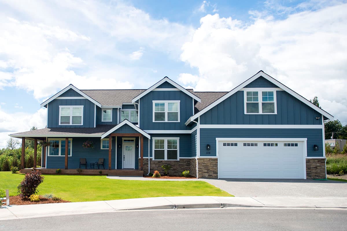 Two-story house plan exterior with gabled dormers, wraparound porch, and attached three-car garage.