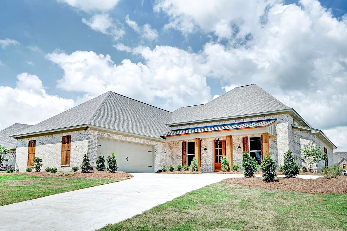 House plan exterior featuring a one-story, brick facade, a front porch with wood columns, and a two-car garage. Overcast sky.