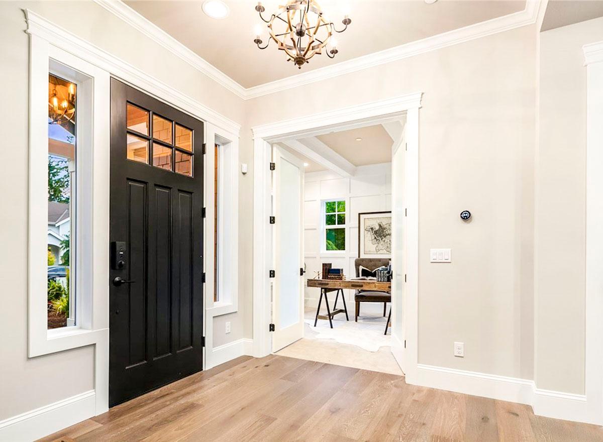 Interior view of home entryway with black paneled door, sidelights, and doorway to a home office with desk and chair.