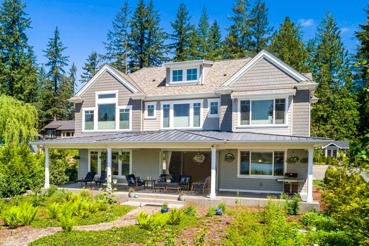 Two-story house plan exterior with wide covered porch, multiple gables, dormer window, and shingle siding.