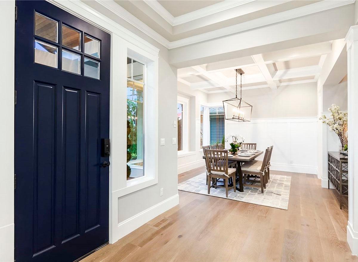 Interior view of dining room with coffered ceiling, dark wood table and chairs, and a dark blue front door.
