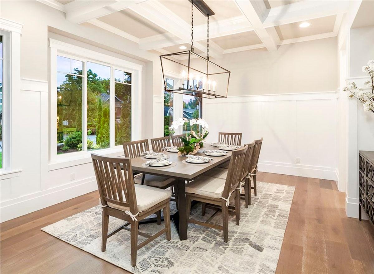 Dining room with coffered ceiling, large windows overlooking trees, and a table set for eight.