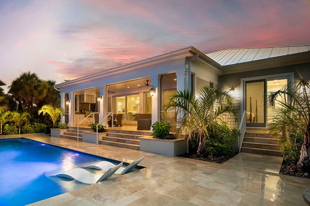 House plan exterior with covered lanai, white columns, metal roof, and sliding glass doors leading to an outdoor living space and pool.