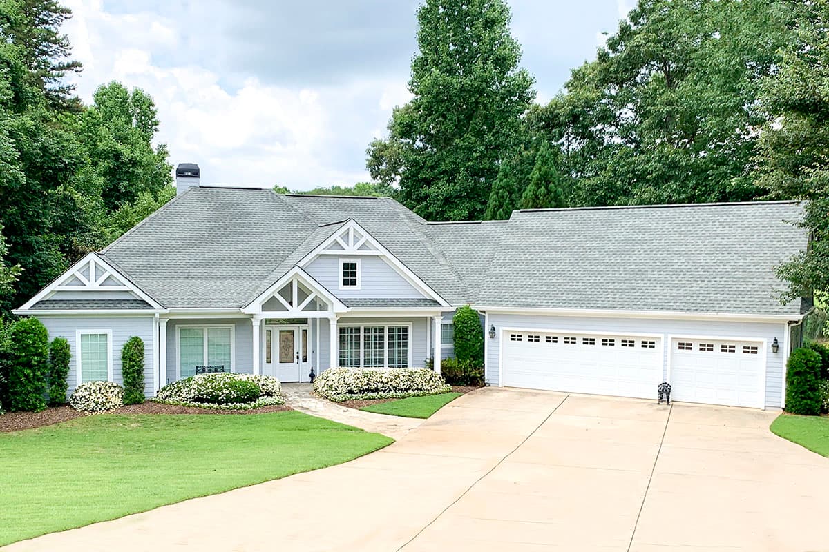 House plan exterior. One-story house with gabled roof, front porch, and three-car garage. Windows are double-hung style with white trim.