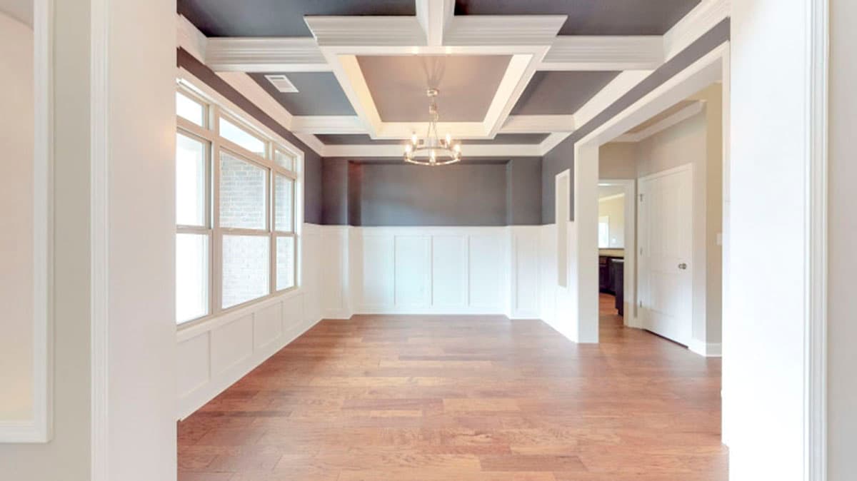 Dining room interior with coffered ceiling, wainscoting, large windows, and hardwood floors.