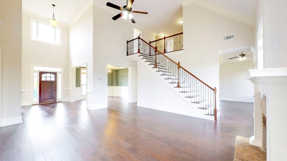 Interior view of a house with a double-height foyer, grand staircase with iron balusters, and wood flooring.
