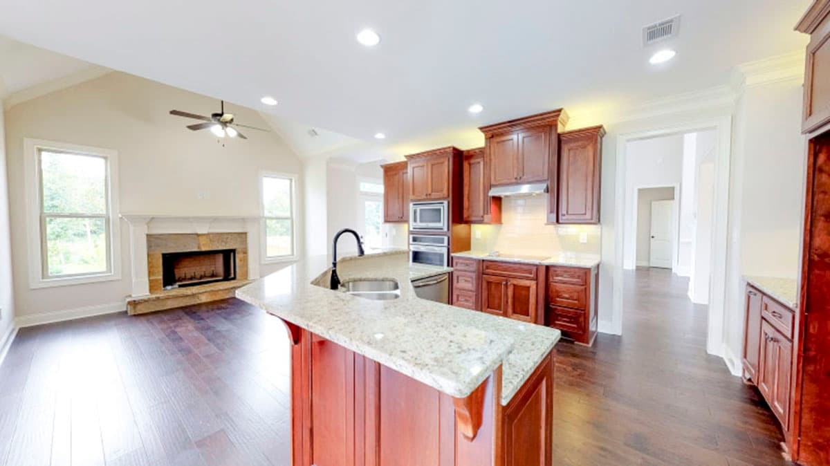 Interior rendering showing a kitchen with a large island and a living area with a stone fireplace and vaulted ceiling.
