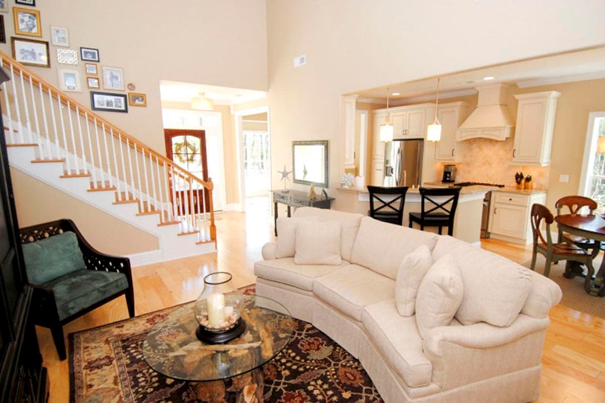 Interior view of open-concept living area with a curved sofa, kitchen island with bar stools, and a staircase with a gallery wall.