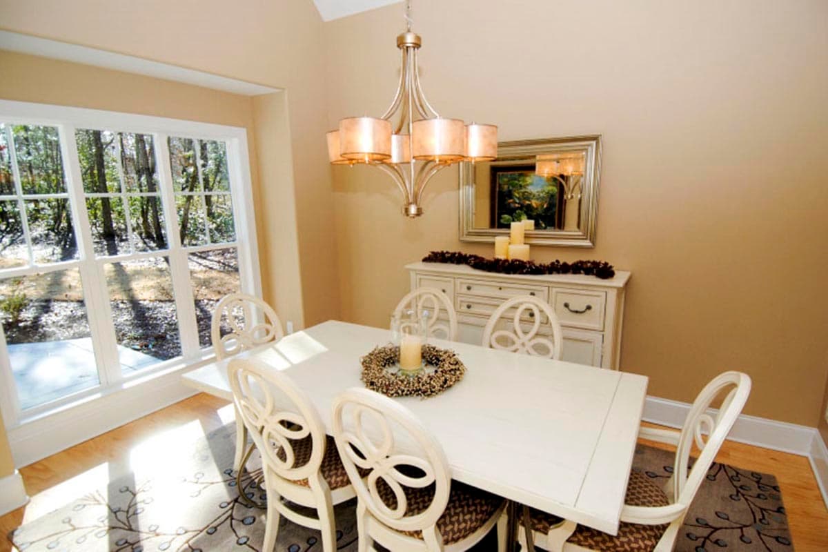 Dining room with white table and chairs, large window overlooking trees, and a buffet with mirror.