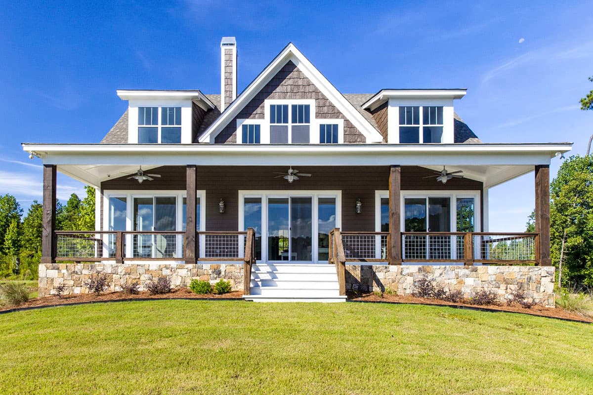 House plan exterior: Two-story modern farmhouse with wide covered porch, stone foundation, gables, dormers, and shake siding.