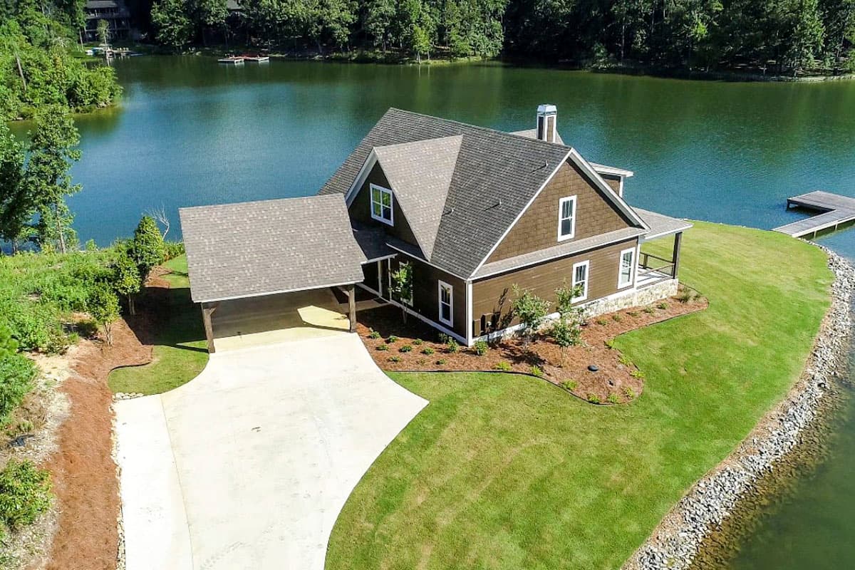 House plan exterior of a two-story home with a detached carport, front porch, and varied rooflines situated by a lake.