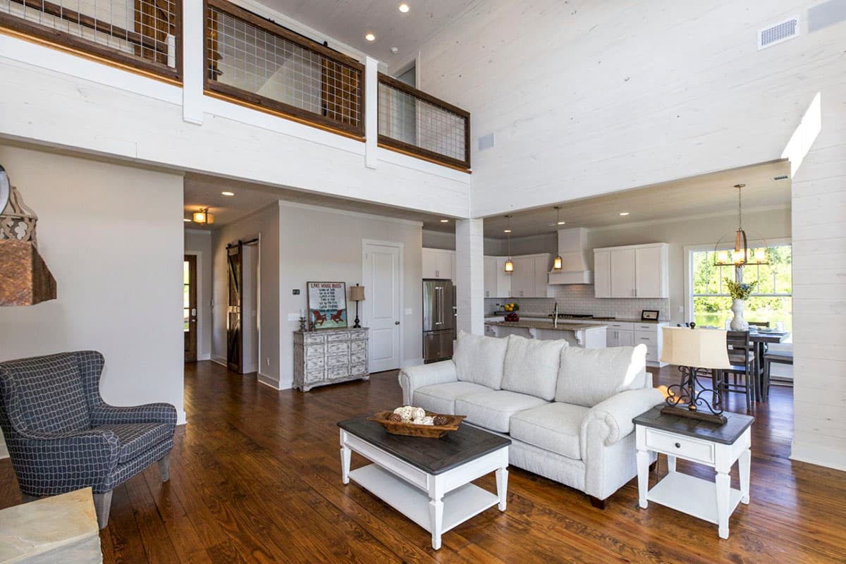 Open-concept living area with vaulted ceilings, a loft overlook with wire railings, and a visible kitchen and dining space.