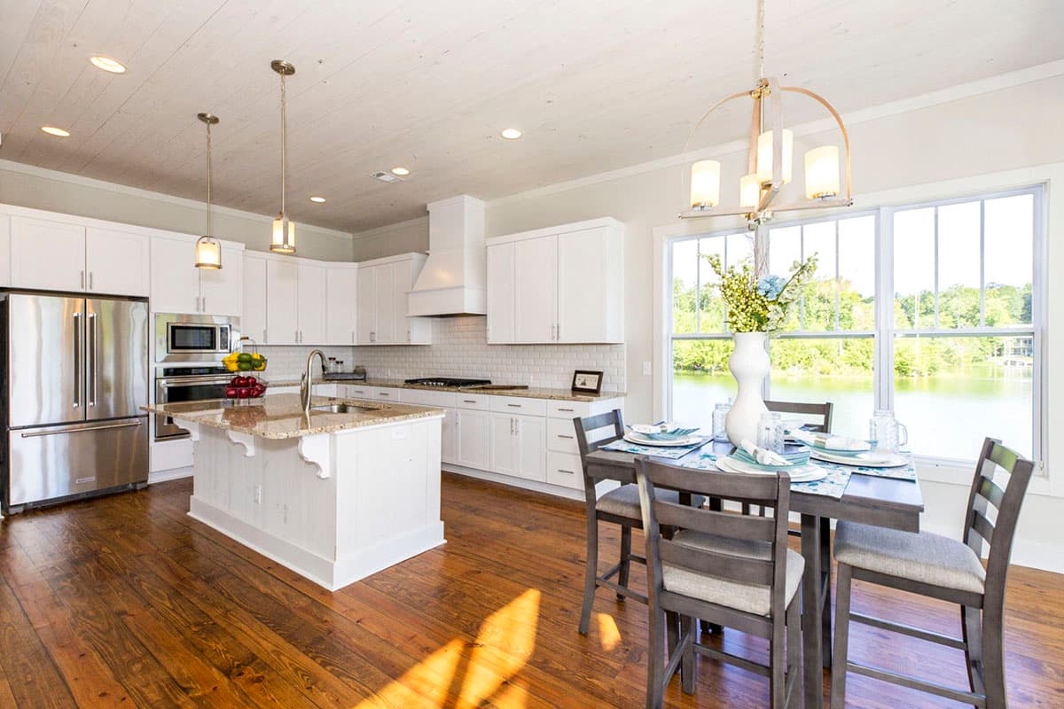 Open-concept kitchen and dining area with white cabinets, granite island, stainless steel appliances, and lake view.
