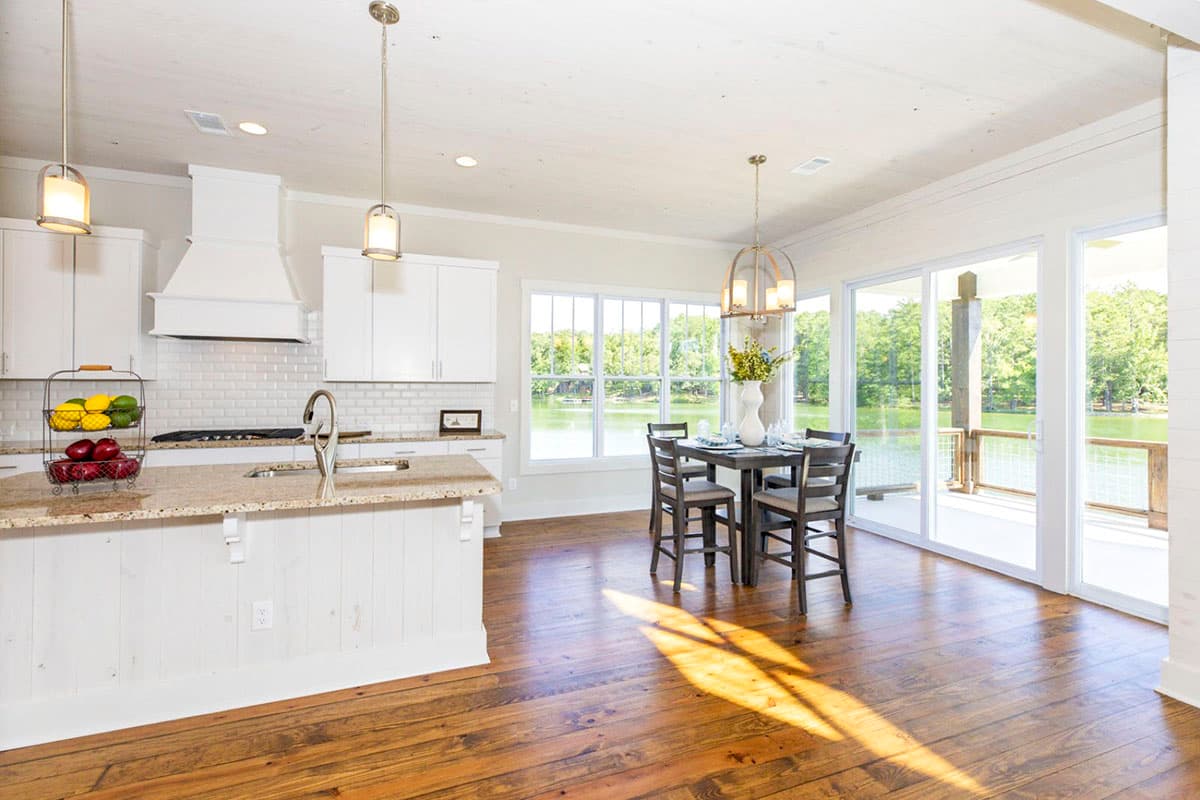 Open concept kitchen and dining area with island, subway tile backsplash, and large windows overlooking a lake.