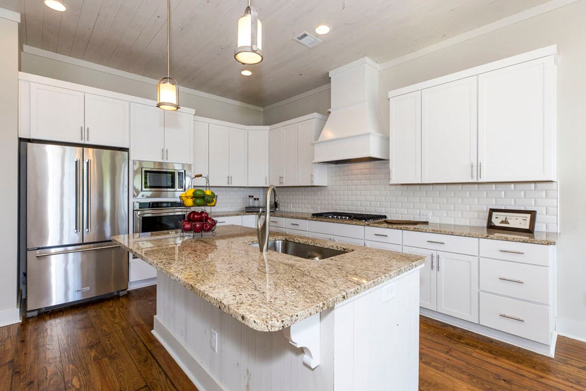 Kitchen featuring white cabinets, granite island with sink, stainless steel appliances, and subway tile backsplash.