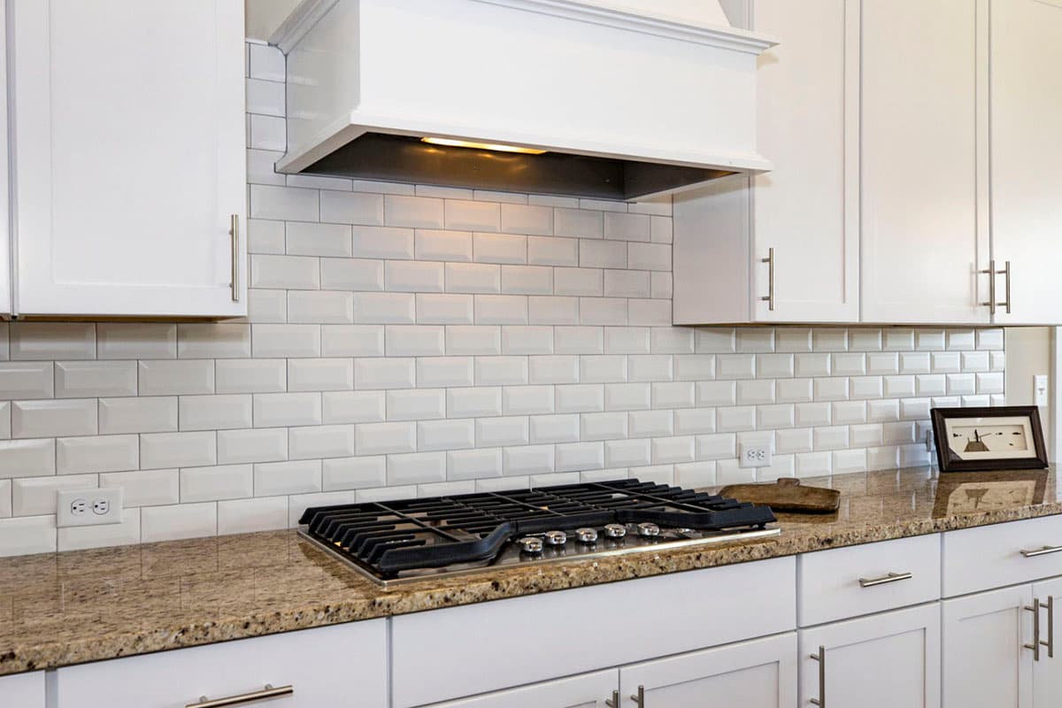 Kitchen interior with white subway tile backsplash, granite countertop, gas range, and white cabinets.