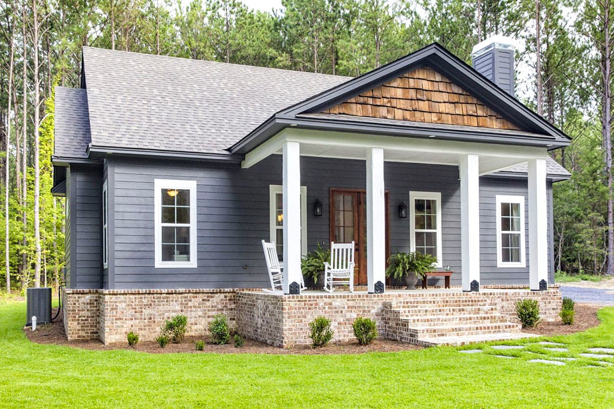 House plan exterior: Modern Farmhouse style, one story, with a covered front porch, wood shingle gable detail, and brick foundation.