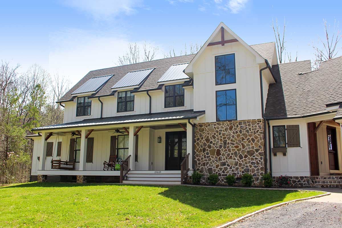 Modern Farmhouse house plan exterior with wrap-around porch, metal roof dormers, stone wainscoting, and double-height windows.
