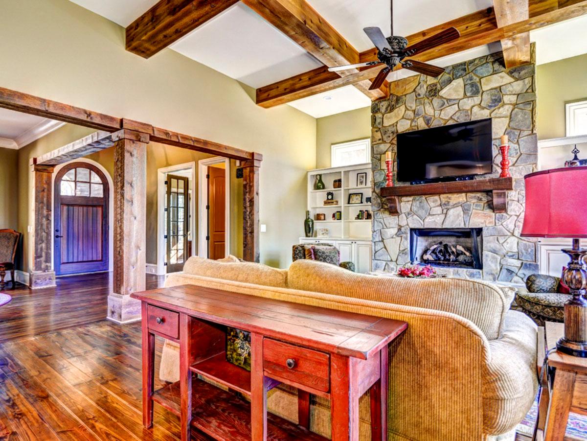 Great room with stone fireplace, exposed wood beams, vaulted ceiling, and arched entry.