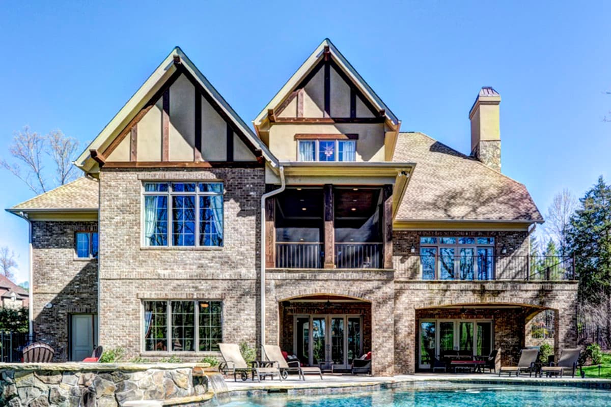House plan exterior: three-story brick home with prominent gables, a covered balcony, and arched lower-level openings.