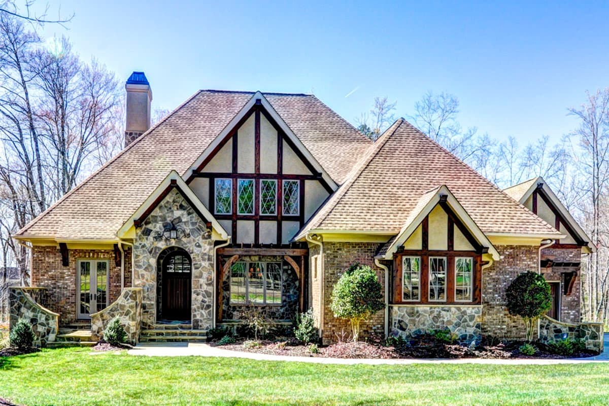 House plan exterior. Tudor style, two-story home with multiple gables, stone accents, and wood trim detailing. Features a chimney.