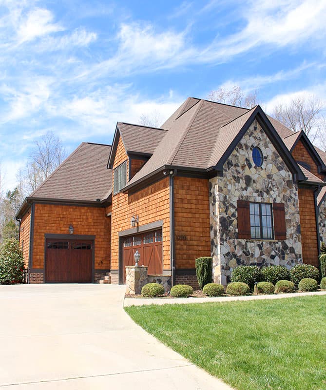 House plan exterior with wood shingle siding, stone facade, multi-level rooflines, and a side-entry garage.