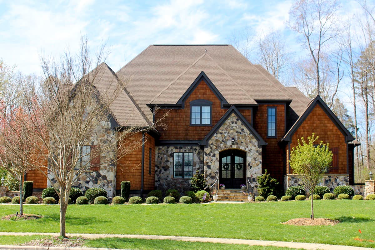 House plan exterior. Two-story home with Craftsman-style elements, stone archway over front door, multiple gables, and cedar shake siding.