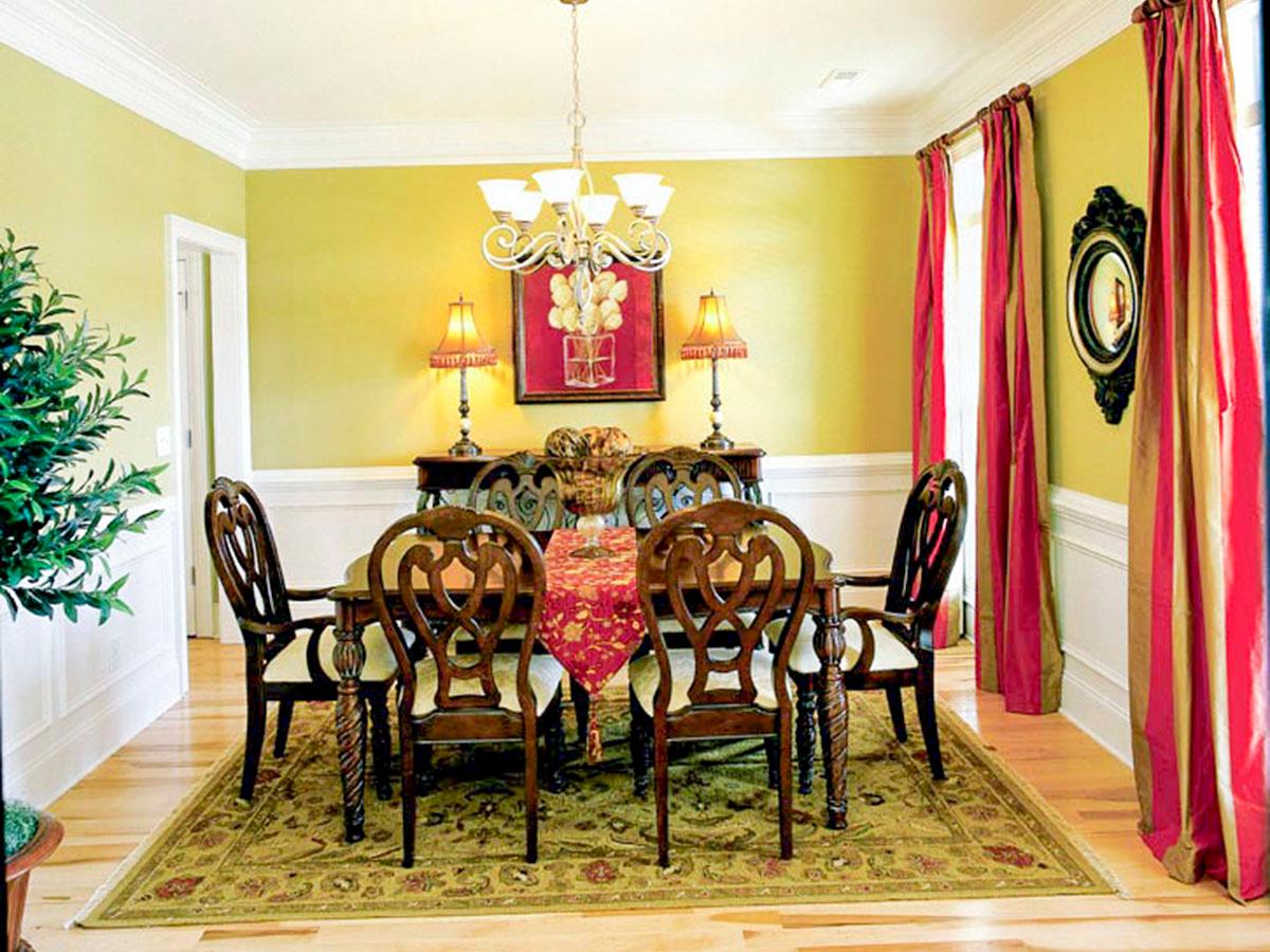 Dining room with wood table, chairs, ornate rug, chandelier, and red striped curtains.