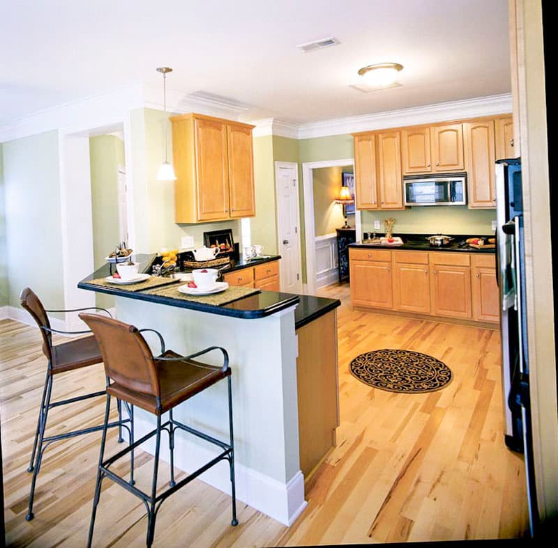 Kitchen with light wood cabinets, black countertop island with bar stools, and hardwood floors.