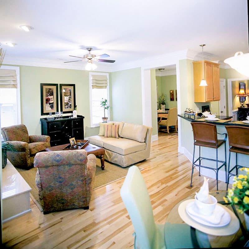Living room with sofa, chairs, coffee table, and dining area visible beyond. Kitchen island with stools and cabinets also shown.