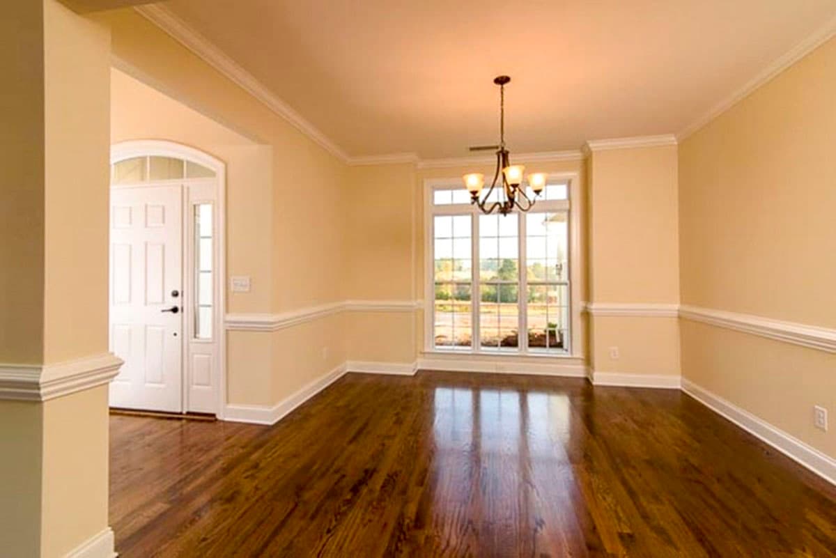 Interior view of a dining room with a large window, crown molding, chair rail, and entry door.
