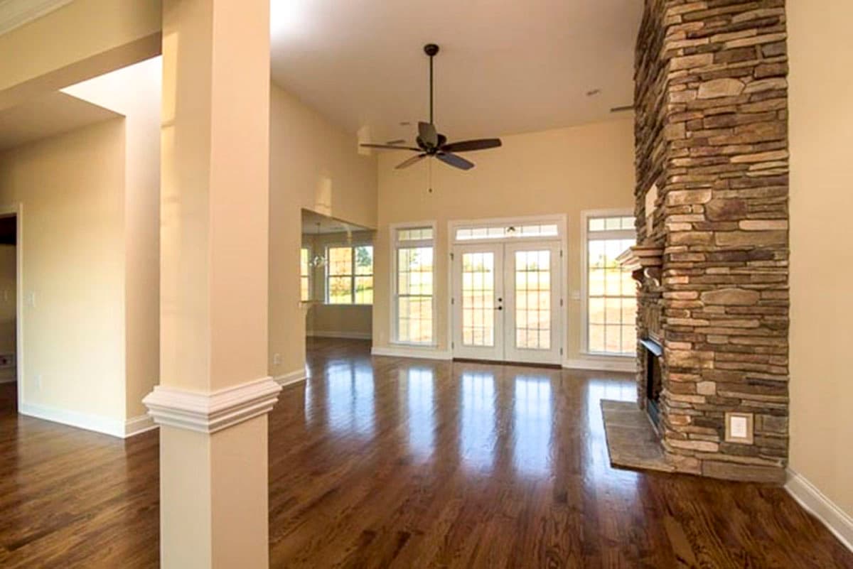 Interior rendering of great room with vaulted ceiling, stone fireplace, ceiling fan, and French doors.