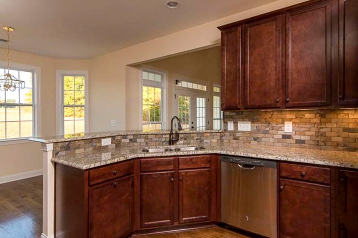 Kitchen with dark wood cabinets, granite counters, multi-colored tile backsplash, stainless steel dishwasher, and bay windows.