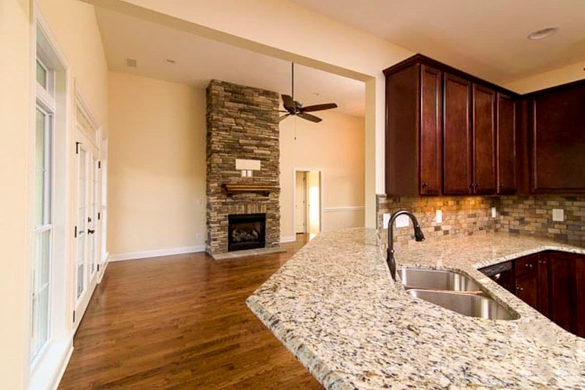 Interior view showing kitchen with granite countertops and a living area with stone fireplace and French doors.