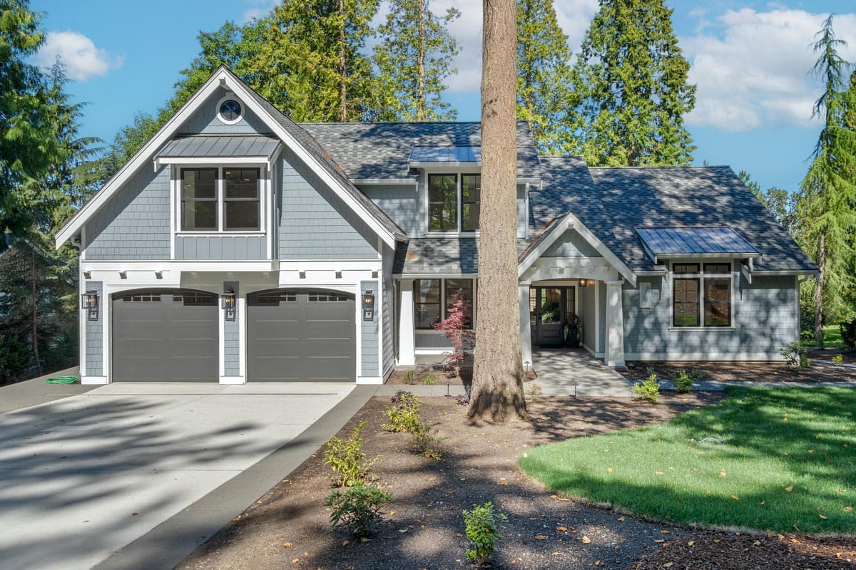 Craftsman style house plan exterior with two stories, a two-car garage, multiple gables, and a front porch. Shingle siding visible.