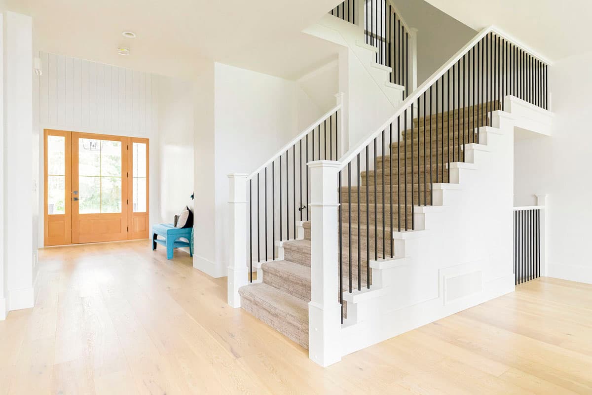 Interior view of a hallway with double wood doors, a light wood floor, and a staircase with carpet treads and black balusters.