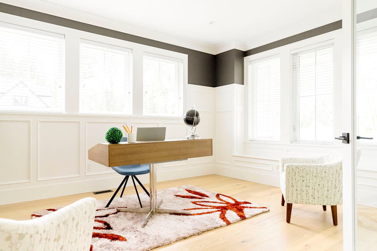 Home office with floating desk, patterned chairs, and large windows with wainscoting.