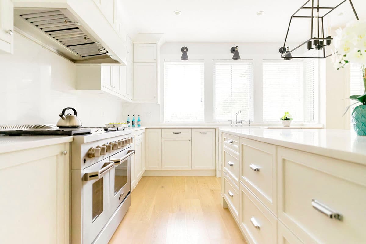 Kitchen with a large range, island with drawers, white countertops, and three windows with blinds.
