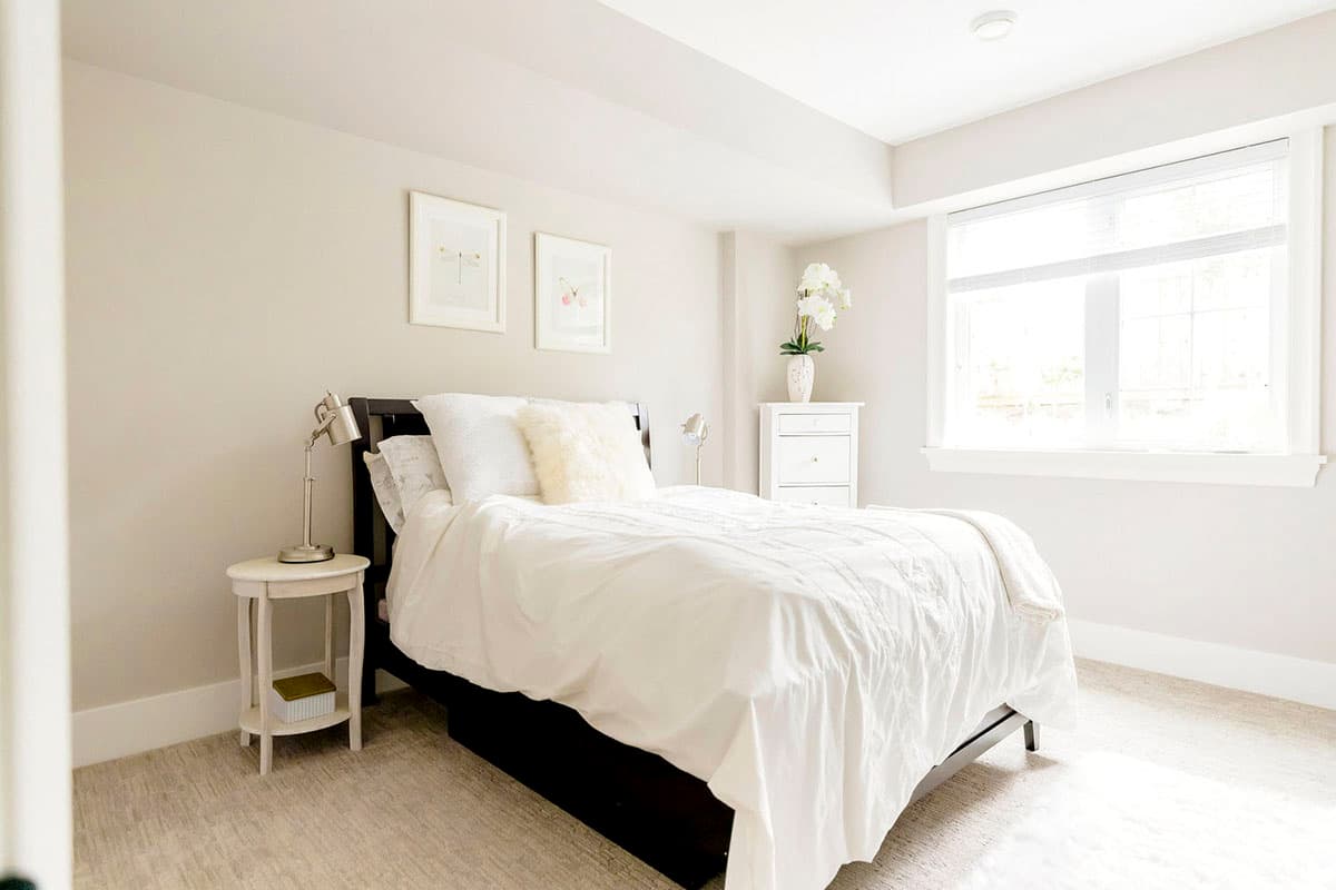 Bedroom with dark wood bed, white bedding, bedside table with lamp, dresser, and large window.