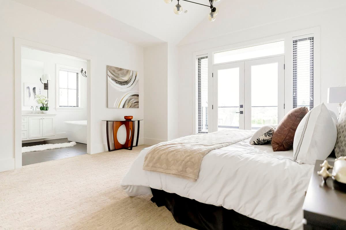 Master bedroom with vaulted ceiling, access to balcony through double doors, and adjoining bathroom.