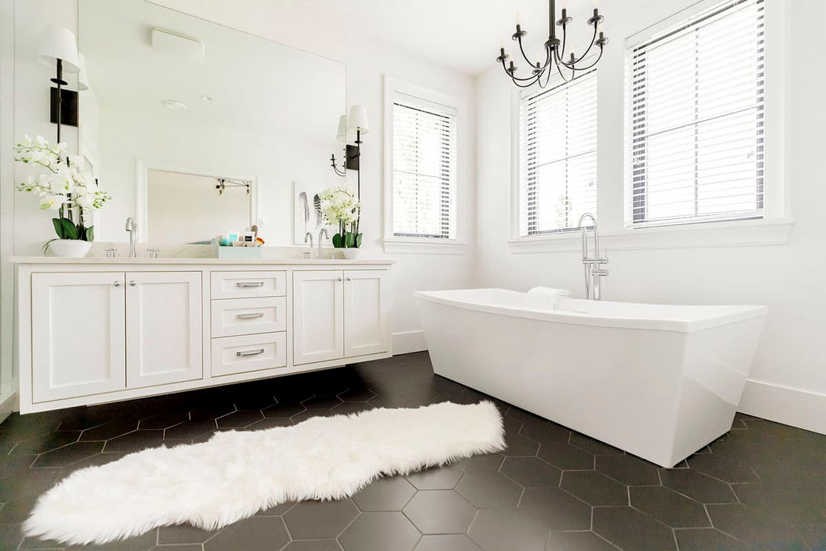 Modern bathroom with freestanding tub, double vanity with marble countertop, hexagonal tile flooring, and chandelier.