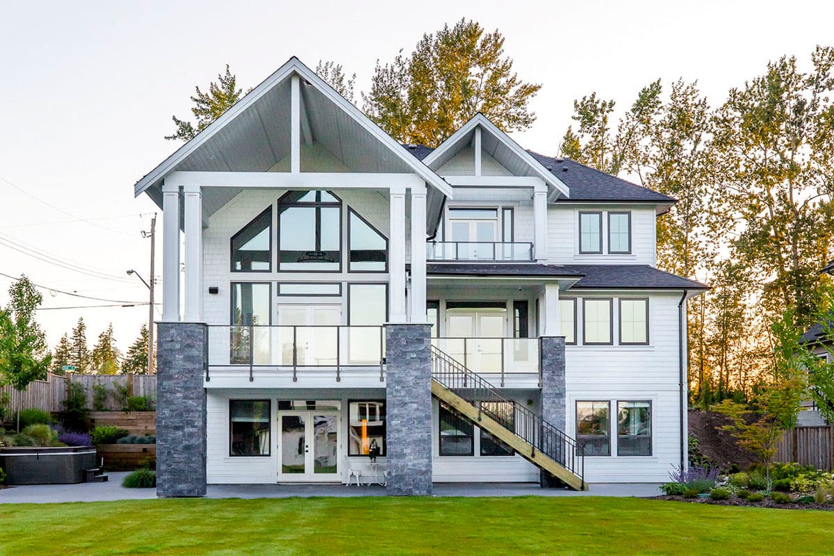 Modern house plan exterior with white siding, dark-framed windows, dramatic gables, and stone accents.