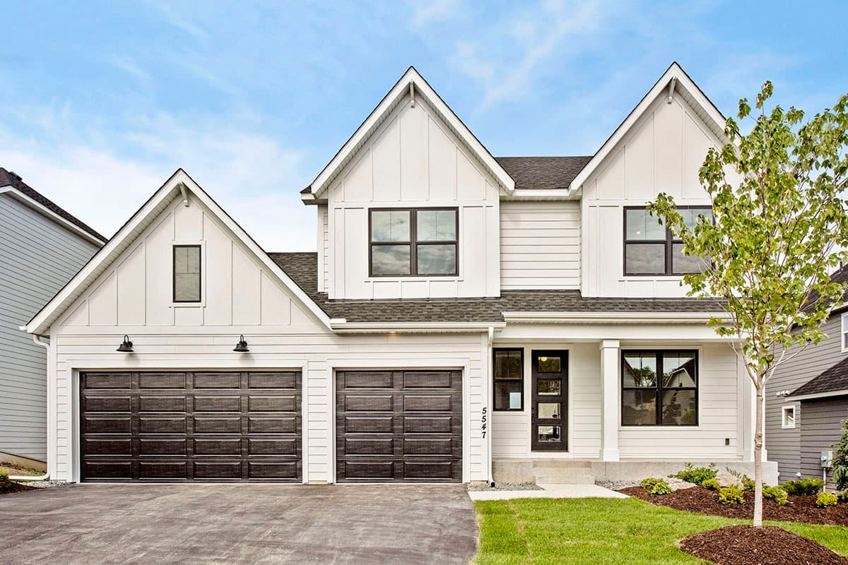 House plan exterior. Modern Farmhouse style, two-story house with gabled rooflines, two garage bays, and a front porch with columns.