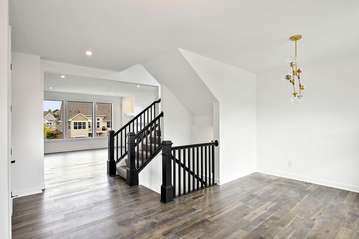 Interior view of a contemporary house with a black spindle staircase, wood floors, and large windows overlooking the exterior.