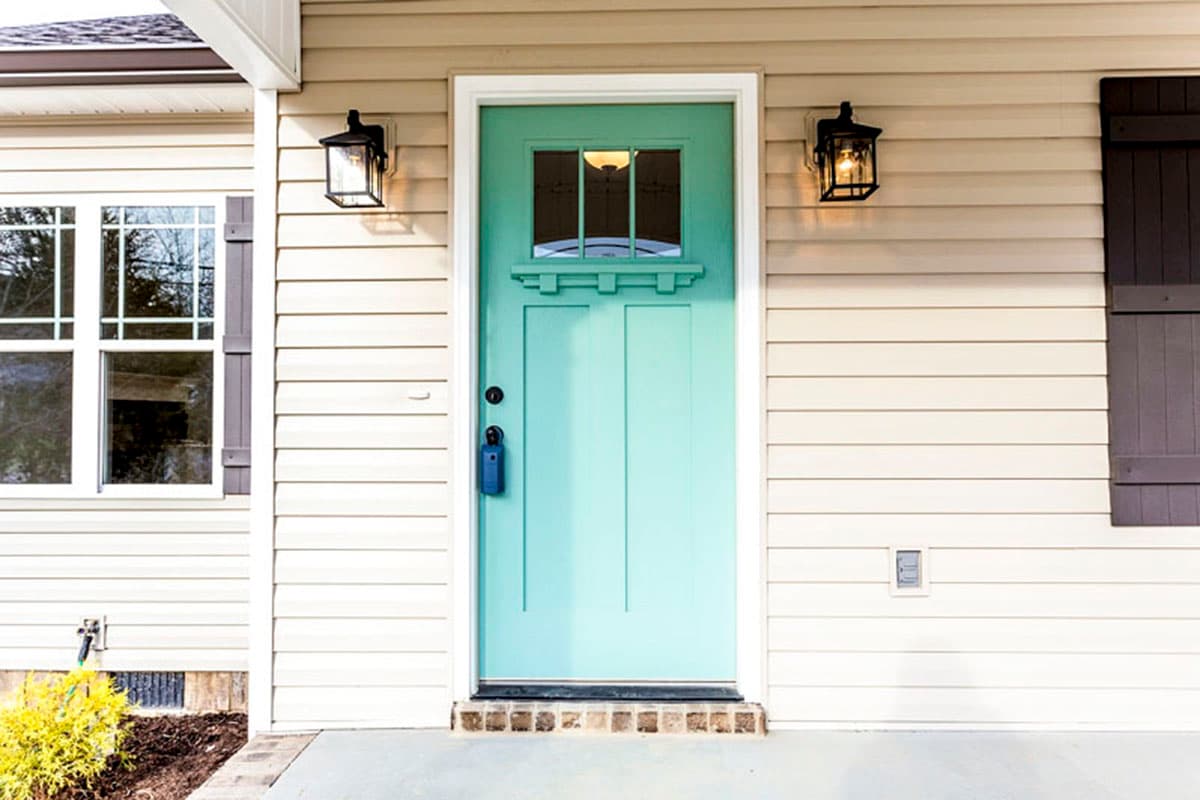 House plan exterior: Teal front door with glass transom, two lanterns, and adjacent window with shutters.